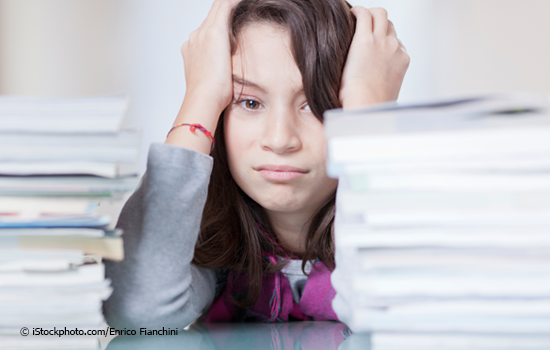 photograph of a bored female student sitting at a table with piles of homework
