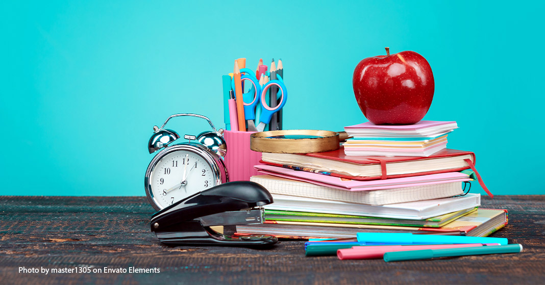 pile of notebooks with apple, stapler, clock, pens, and pencils