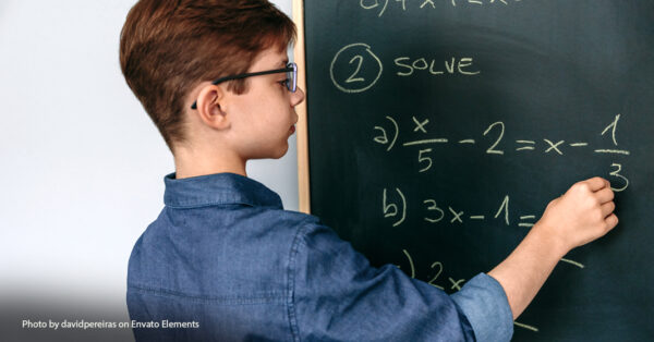 boy writing math equations on chalk board