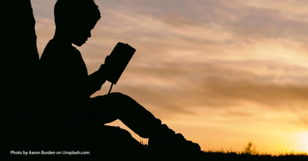 silhouette of a child reading the Bible with sunset in background